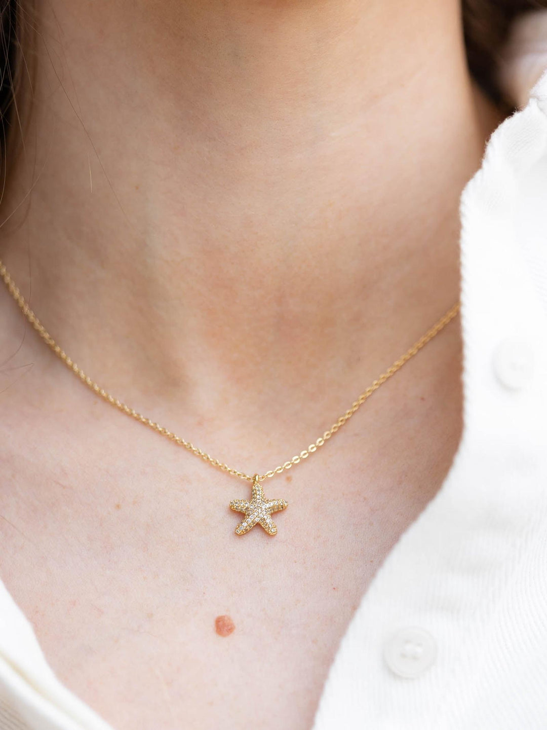 Gold chain necklace with a small, sparkling rhinestone pavé starfish charm on a person&