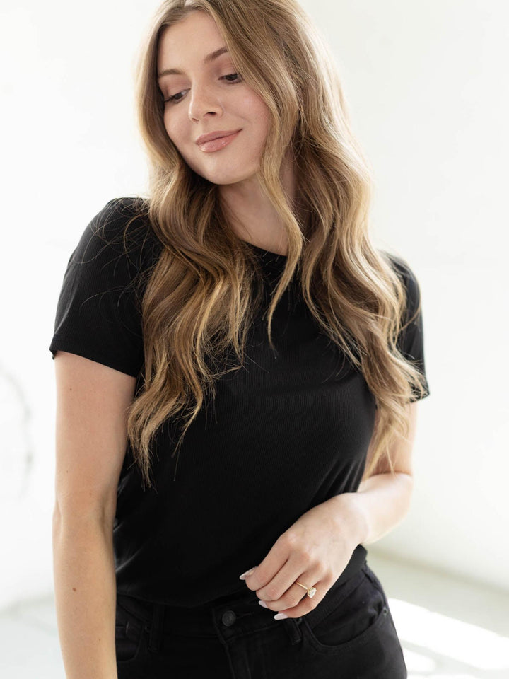 Woman in a black ribbed crew neck tee with short sleeves and a curved hem, looking down.
