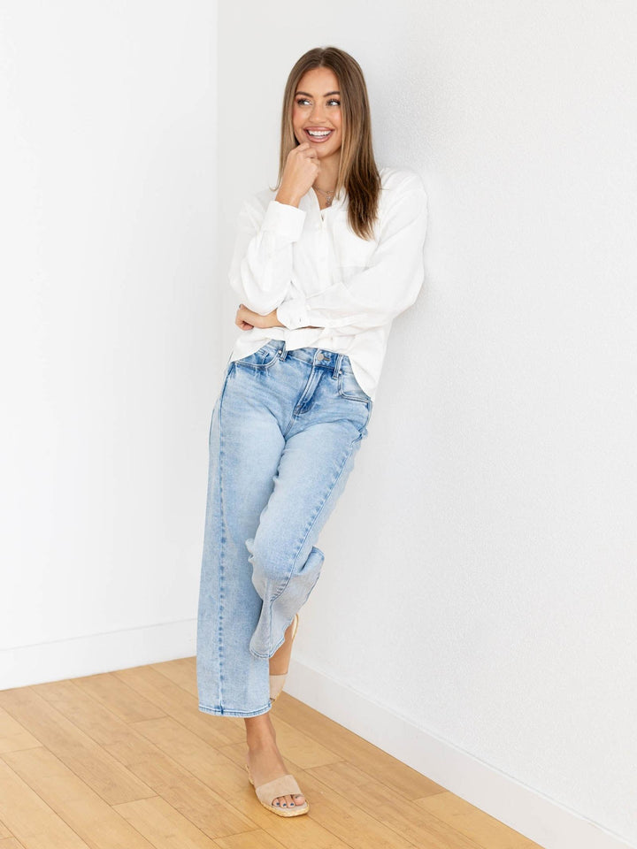 Woman wearing a white sweater and light blue jeans against a white wall.