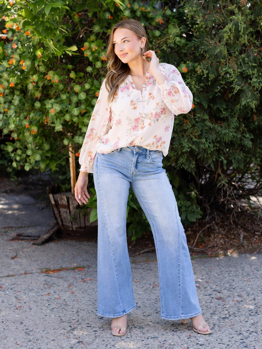 Woman wearing light wash RISEN high rise ankle wide curved seam detail jeans and a floral blouse.