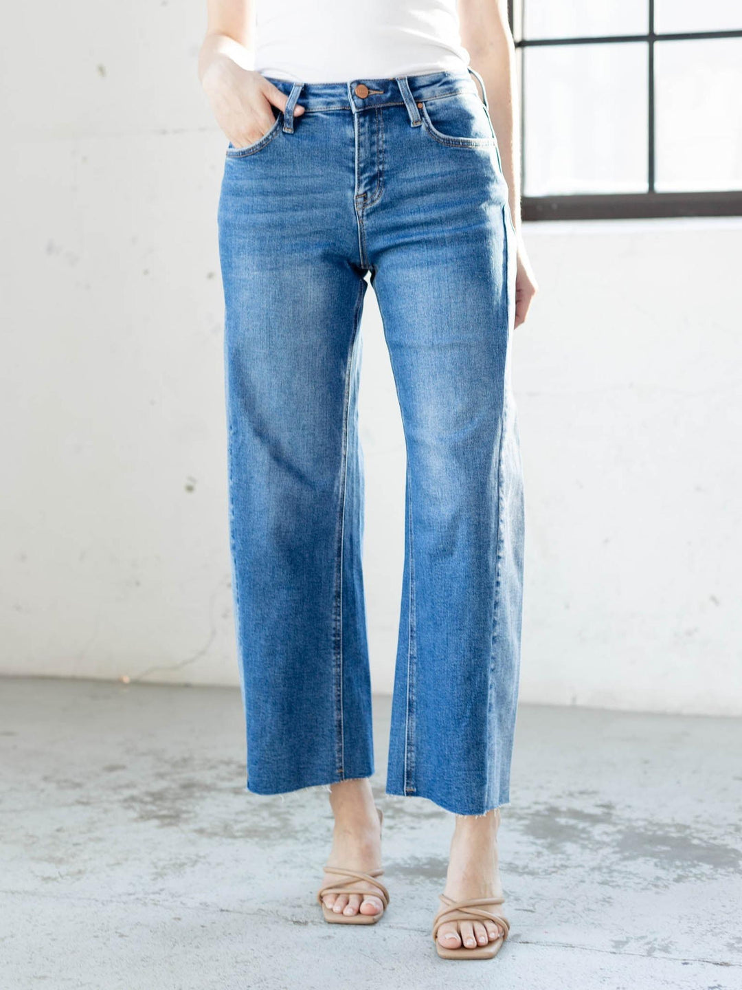 Person wearing blue jeans standing in a minimalistic room with a white wall and concrete floor.