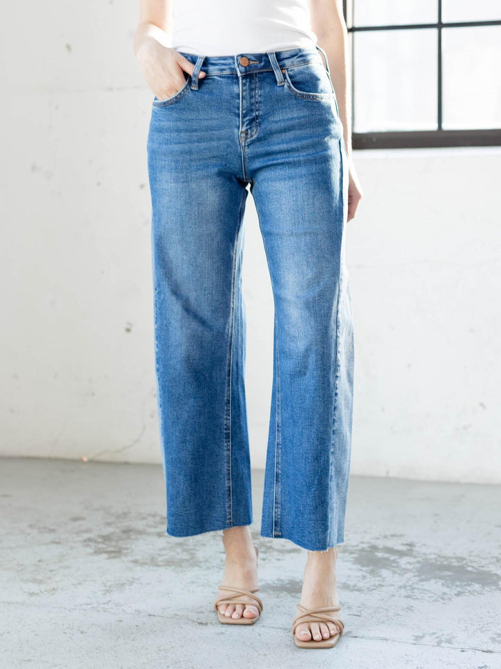 Person wearing blue jeans standing in a minimalistic room with a white wall and concrete floor.