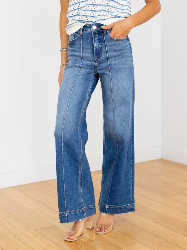 Person wearing blue jeans on a wooden floor with a white wall background