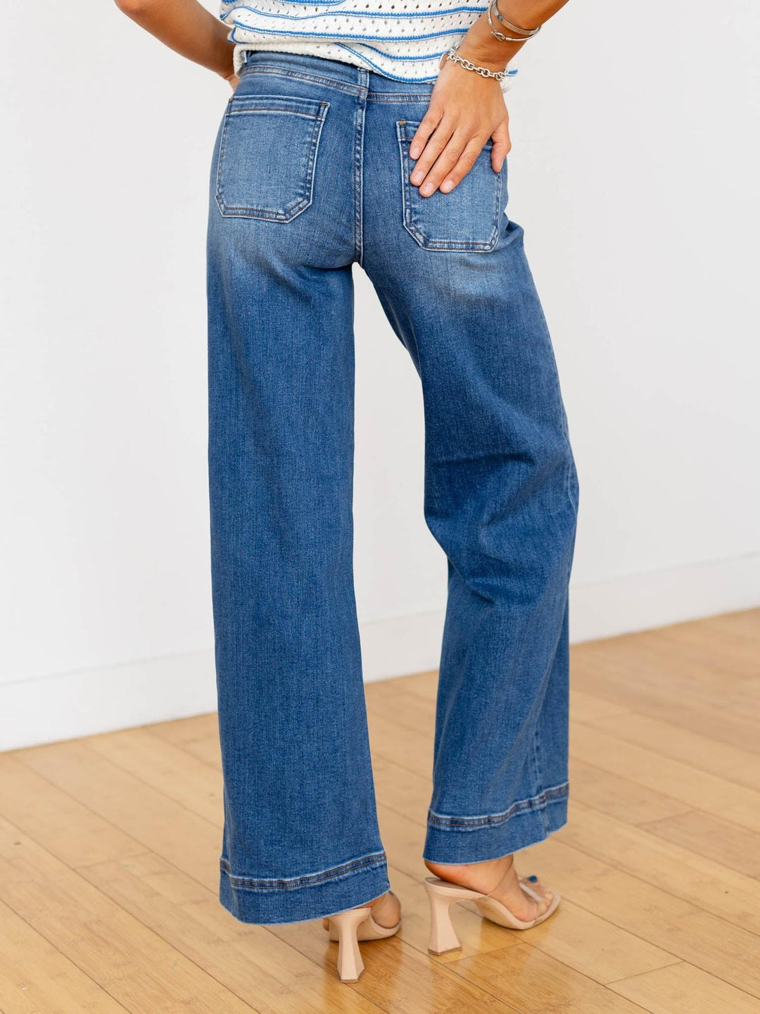 Person wearing blue jeans on a wooden floor with a white wall background