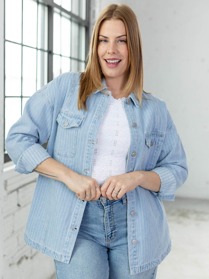 Woman wearing a light blue denim jacket over a white shirt in a bright room.