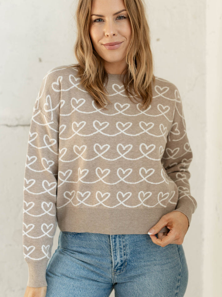 Woman wearing a beige sweater with heart patterns against a white background