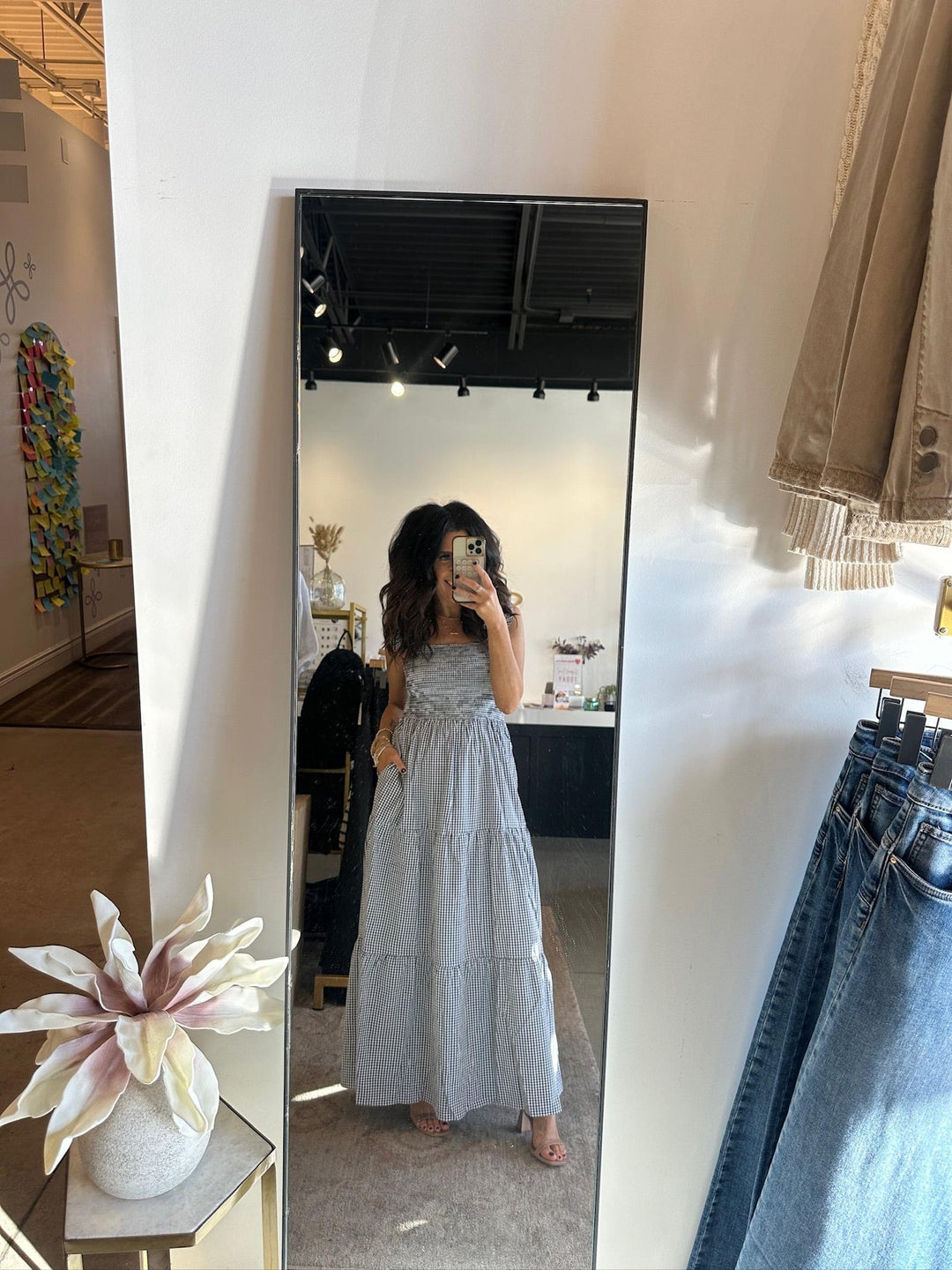 Person taking a mirror selfie wearing a long light blue dress in a store setting.