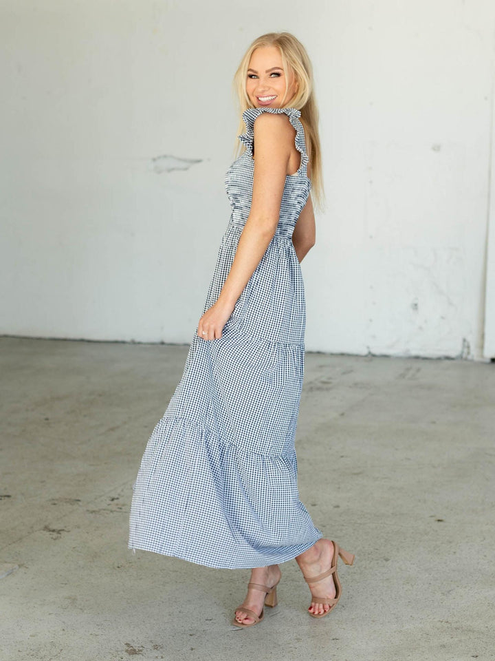 Woman wearing a blue checkered dress against a white wall.