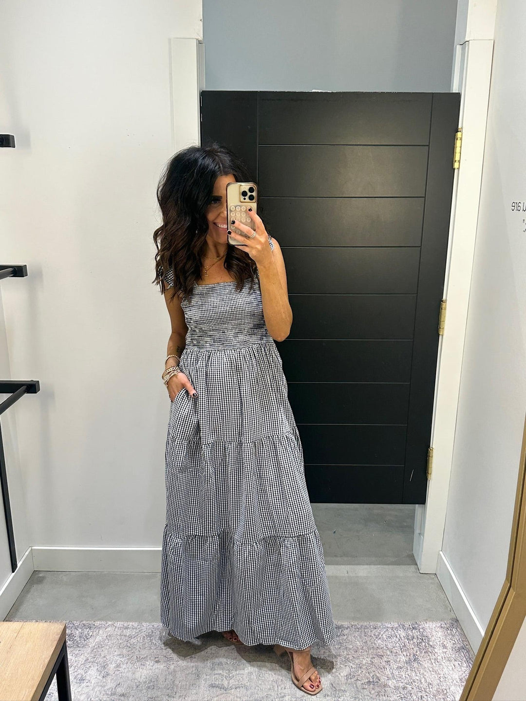 Woman taking a mirror selfie wearing a gray tiered dress in a room with a black wall.