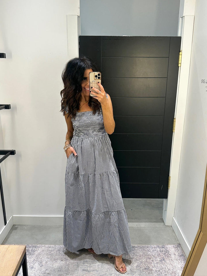 Woman taking a mirror selfie wearing a gray tiered dress in a room with a black wall.