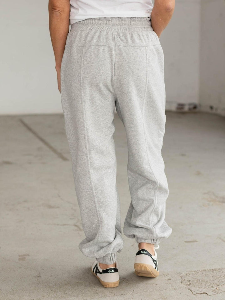 Person wearing gray sweatpants and black and white sneakers in a minimal indoor setting