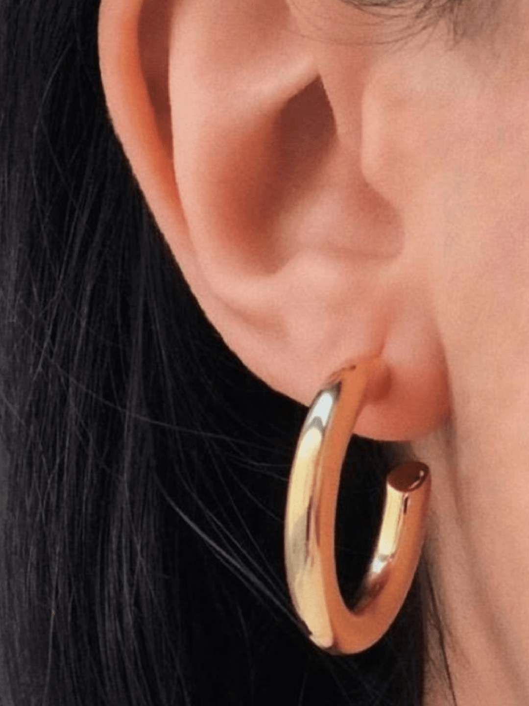 Gold hoop earring worn by a person with dark hair.