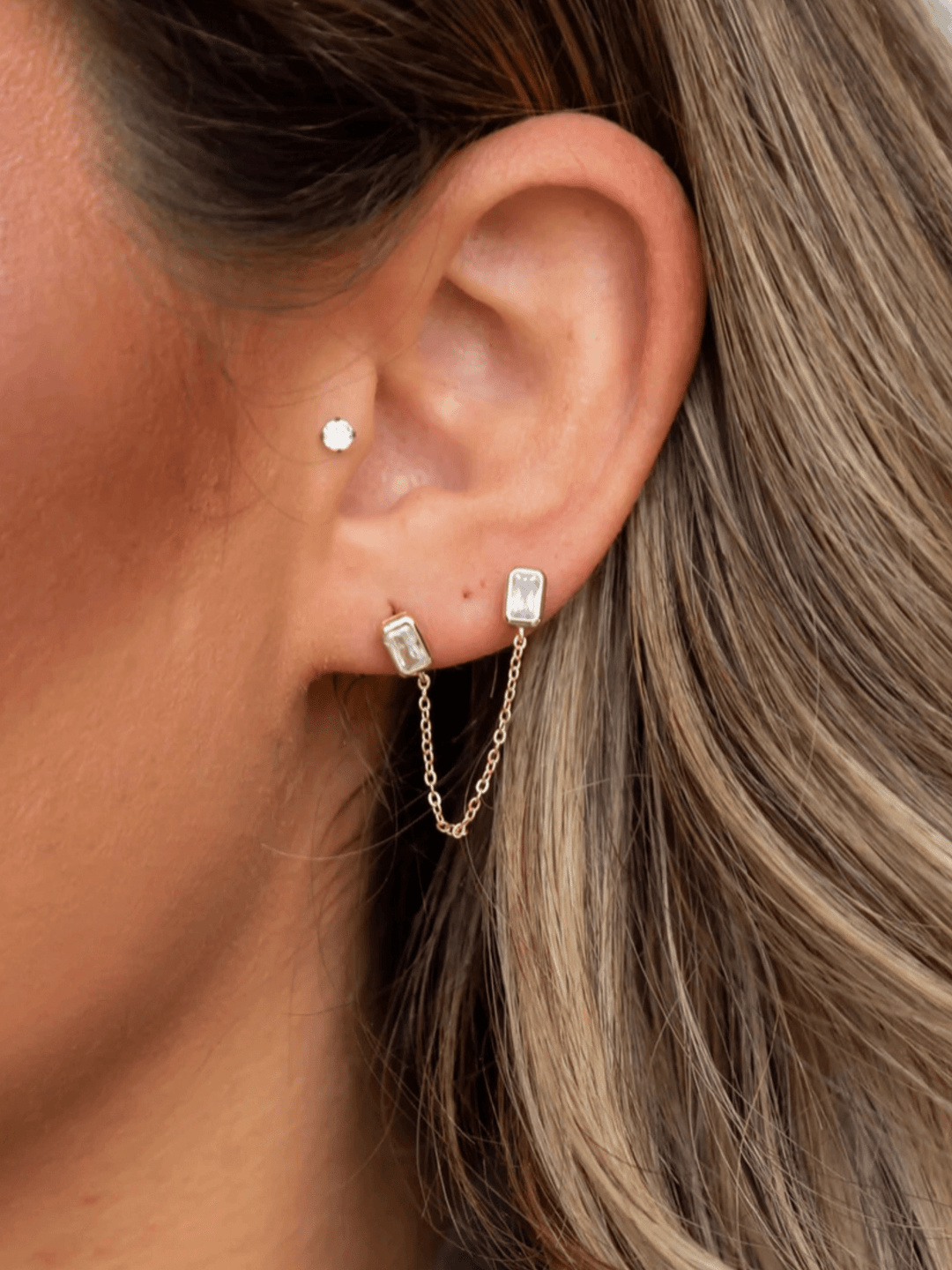 Close-up of an ear wearing gold hoop earrings with small gemstones.