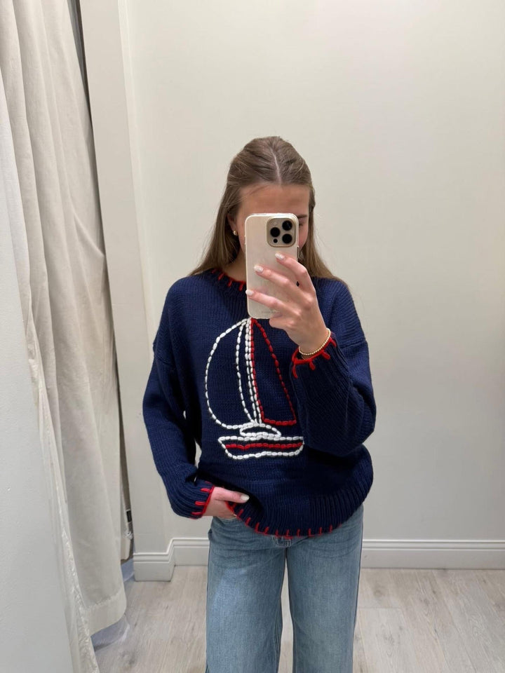 Person wearing a navy sweater with a sailboat design, taking a mirror selfie.
