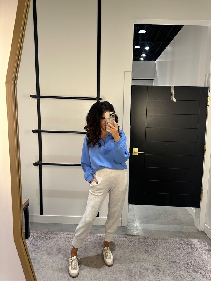 Person taking a mirror selfie wearing a blue shirt and white pants in a room with a black door and white walls.