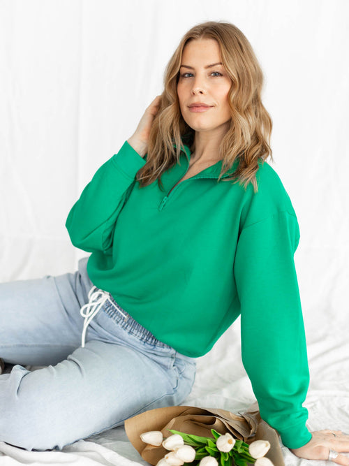 Woman wearing a green blouse and light blue jeans sitting on a white surface with flowers.