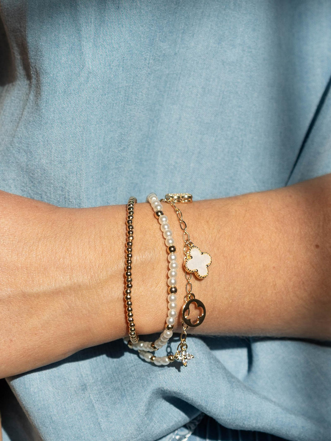 Close-up of a wrist wearing multiple bracelets with a light blue background
