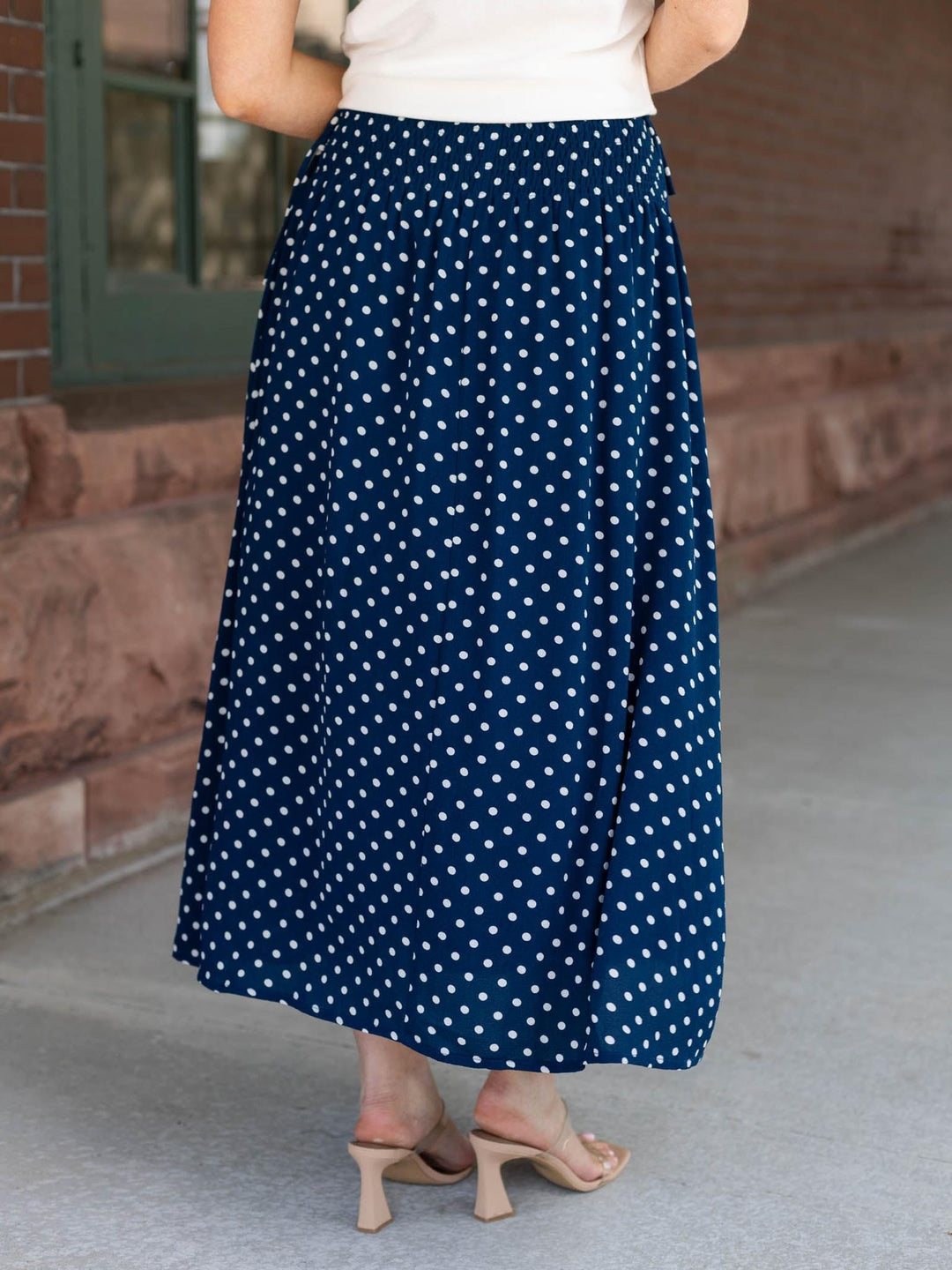 Person wearing a long navy polka dot skirt on a porch.