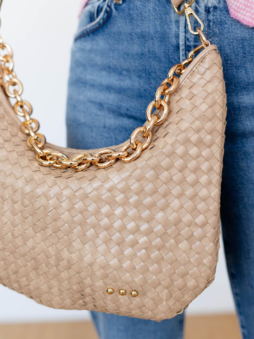 Beige handbag with gold chain strap held by a person wearing blue jeans.