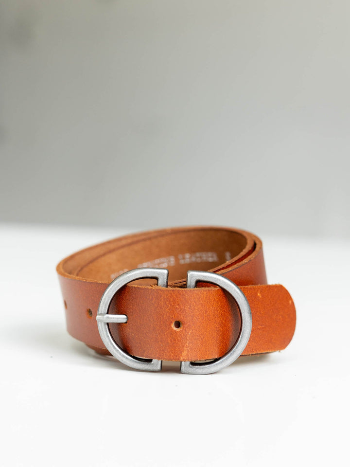 Brown genuine leather belt with a silver D-ring buckle, coiled on a white surface.
