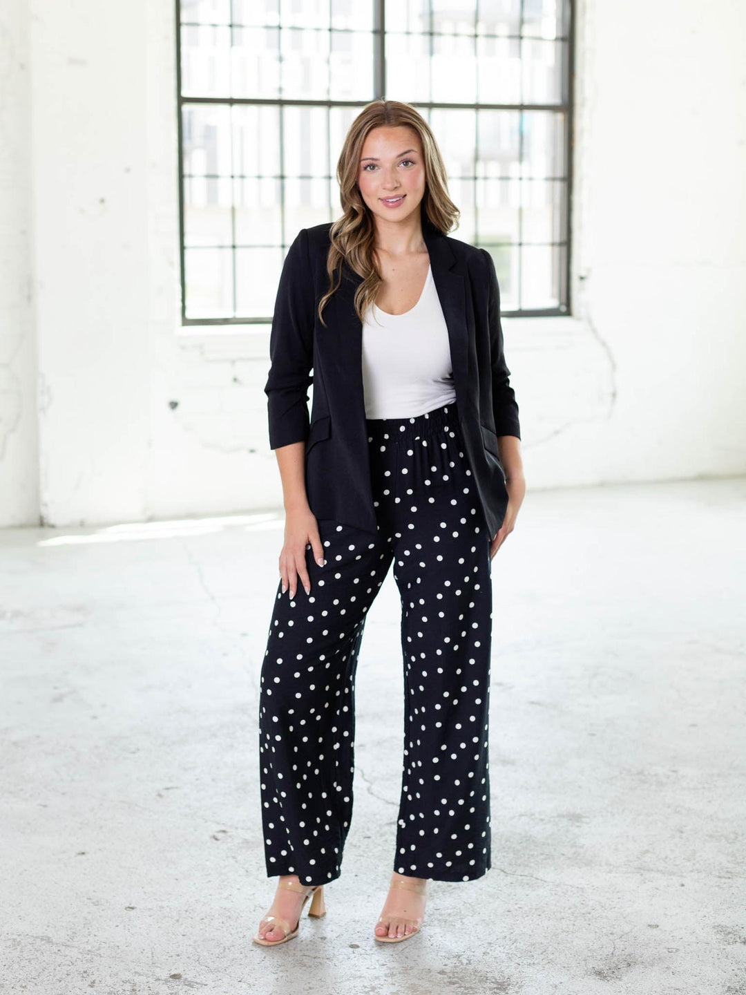 Woman in a black recycled shirred sleeve blazer, white top, and black polka dot pants.