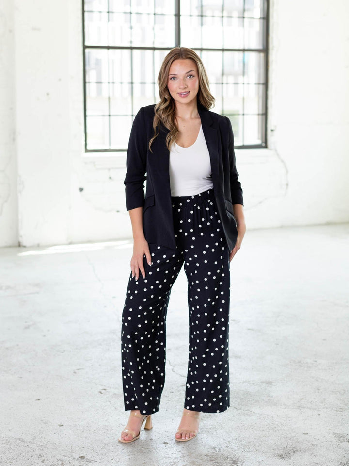 Woman in a black recycled shirred sleeve blazer, white top, and black polka dot pants.