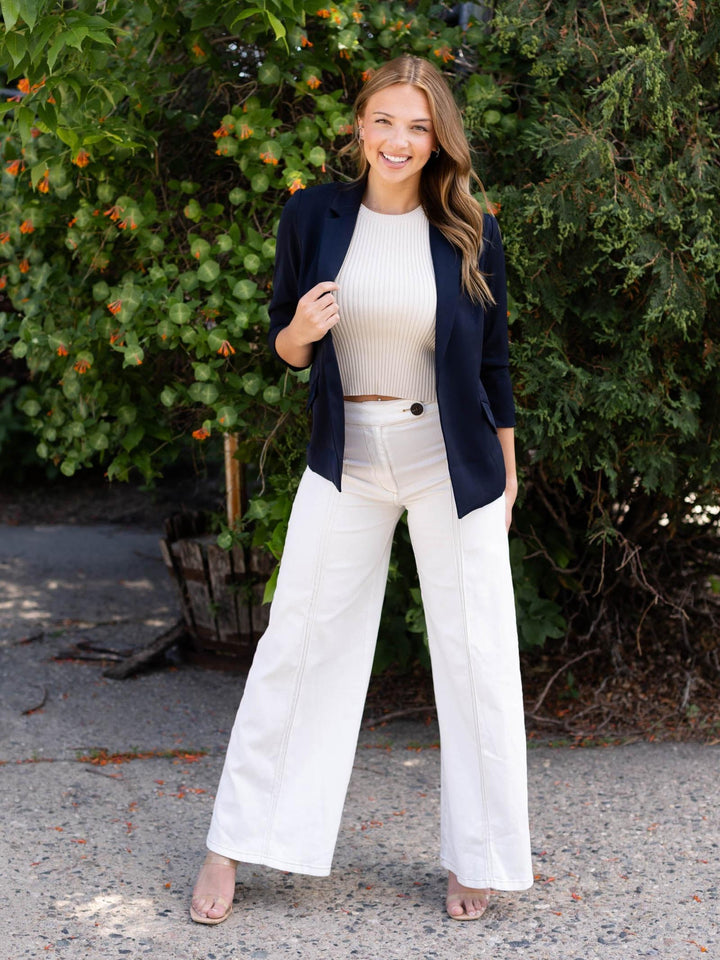 Woman in a navy recycled shirred sleeve blazer, white ribbed crop top, and white wide-leg pants.