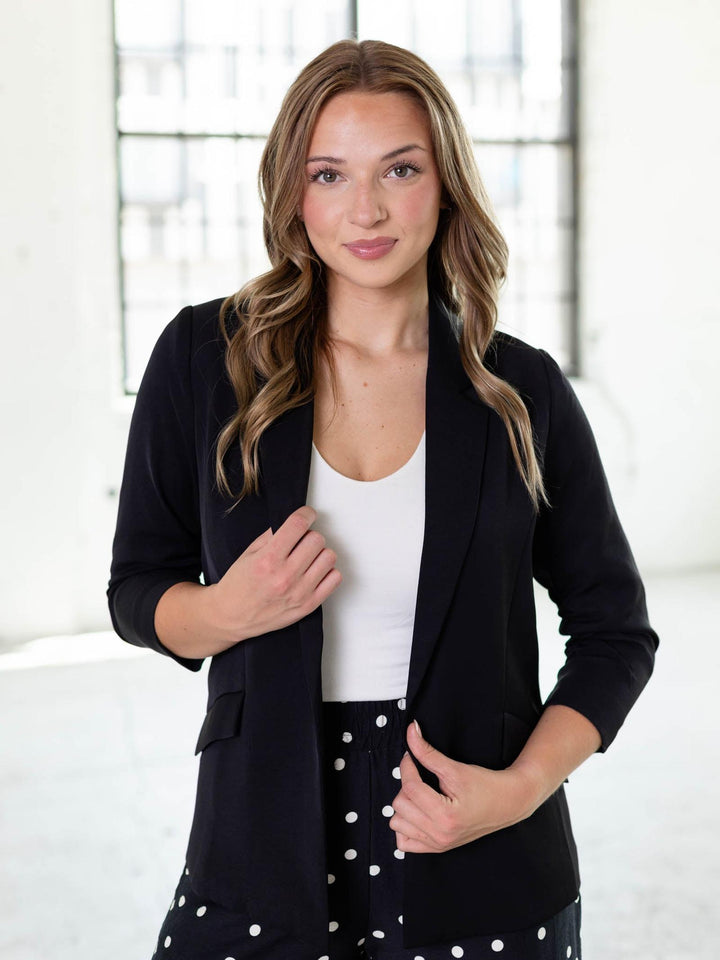 Woman in a black recycled shirred sleeve blazer, white top, and polka dot pants.