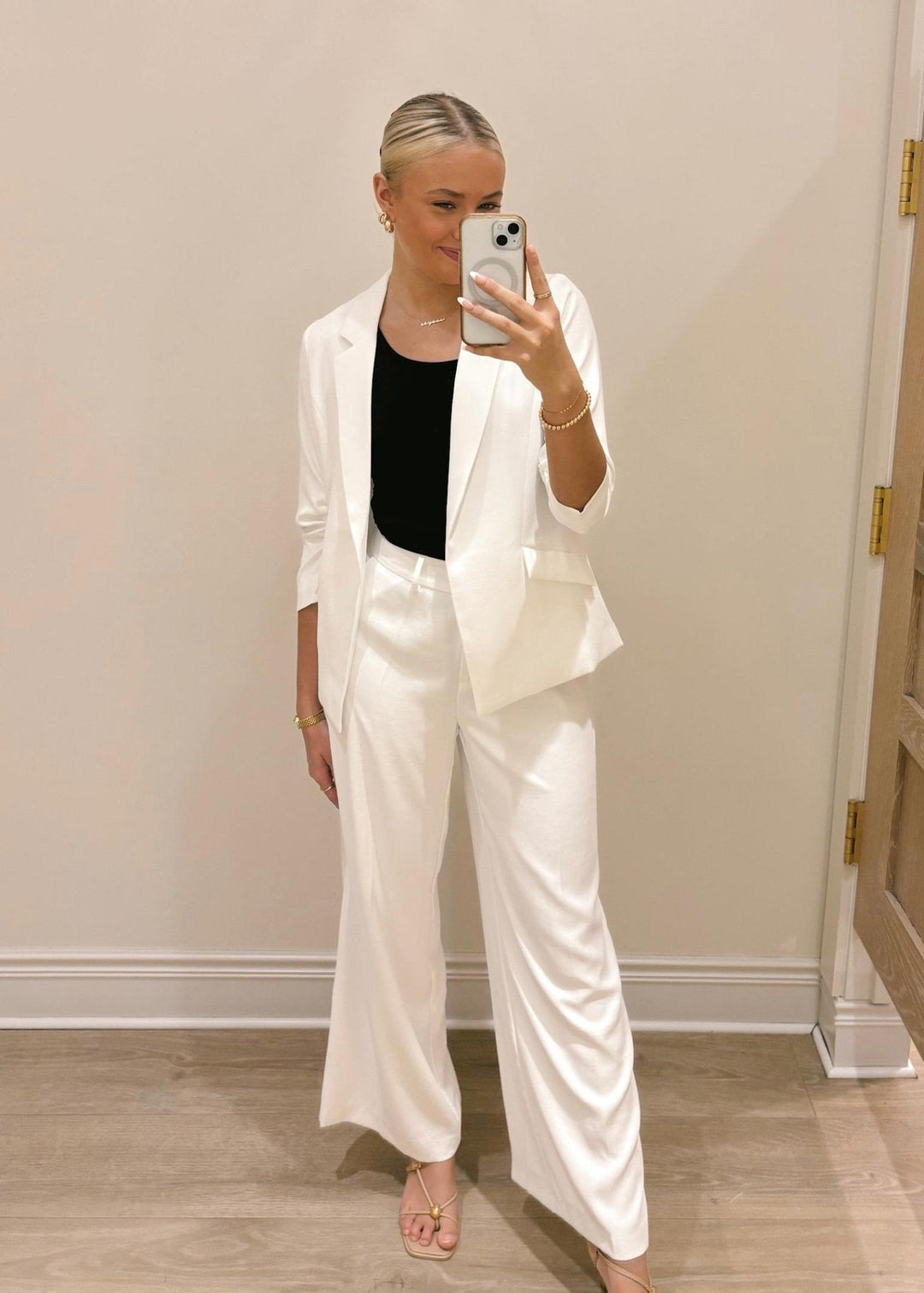 Person wearing a white suit taking a mirror selfie indoors.