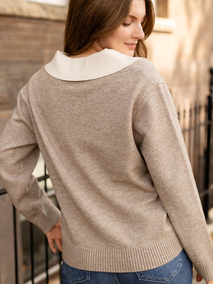 A woman wearing a light beige knit sweater with a contrasting white collar, shown from the back in an outdoor setting.