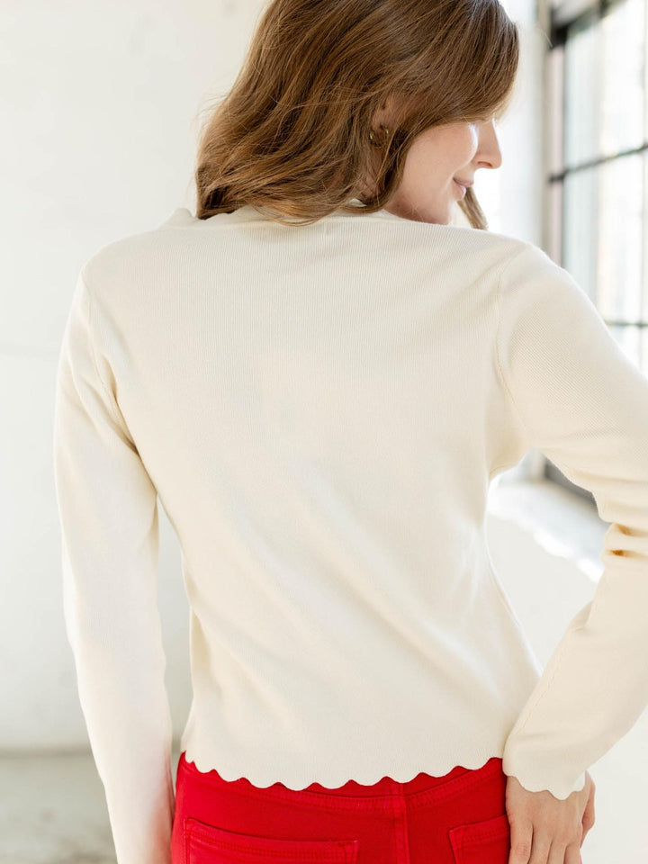 Woman wearing a cream sweater and red pants in a bright room.