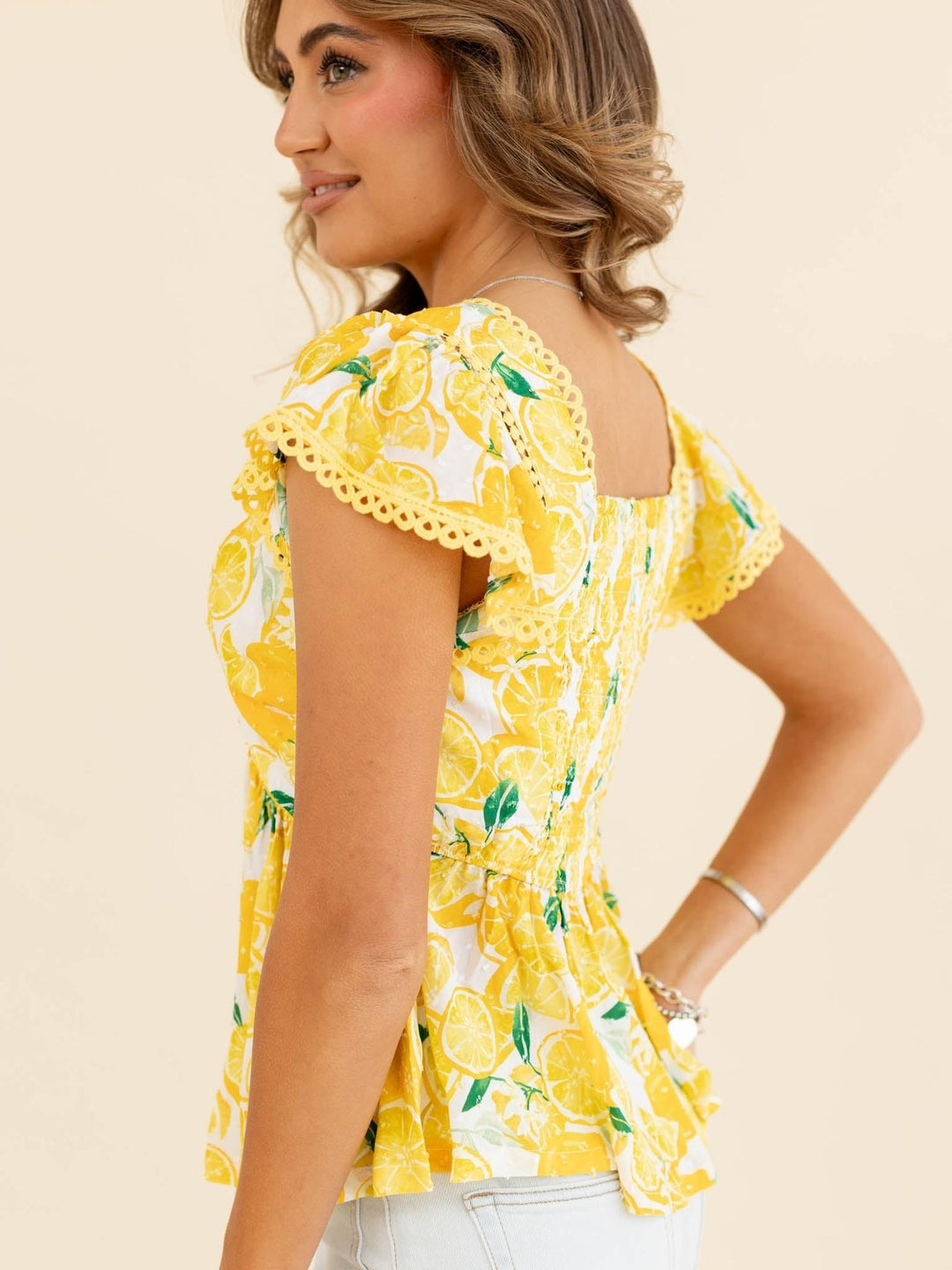 Woman wearing a yellow lemon print top on a beige background