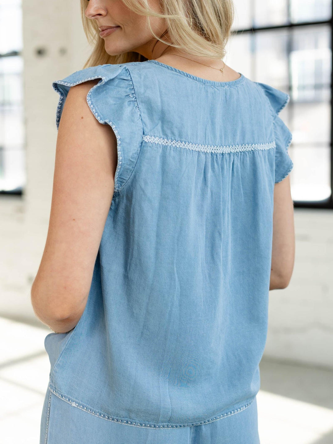 Woman wearing a light blue denim dress with ruffled sleeves in an indoor setting.