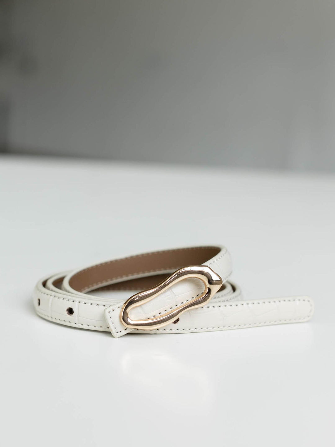 White skinny croco-embossed leather belt with a gold asymmetrical buckle.