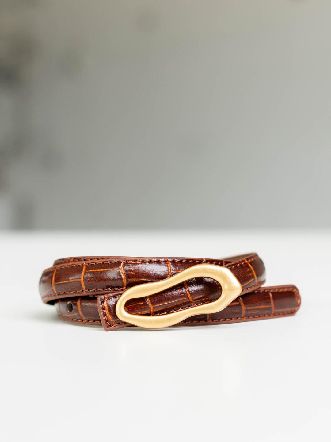 Brown skinny croco-embossed leather belt with a thin asymmetrical gold buckle.