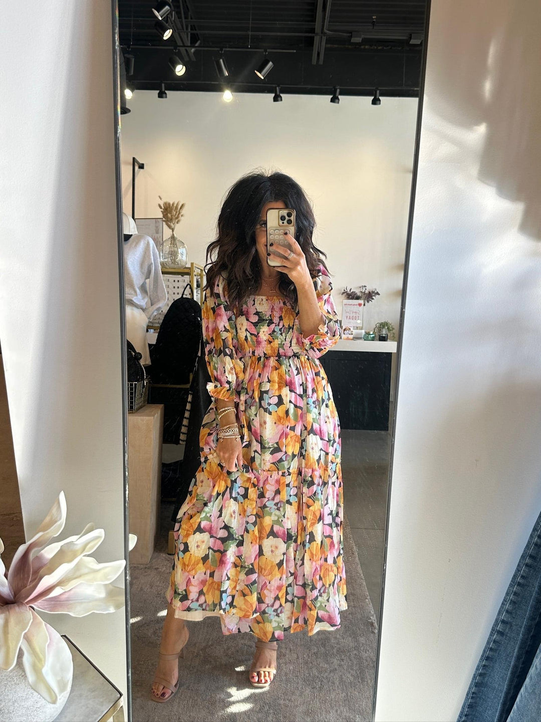 Person wearing a floral dress taking a mirror selfie in a store.