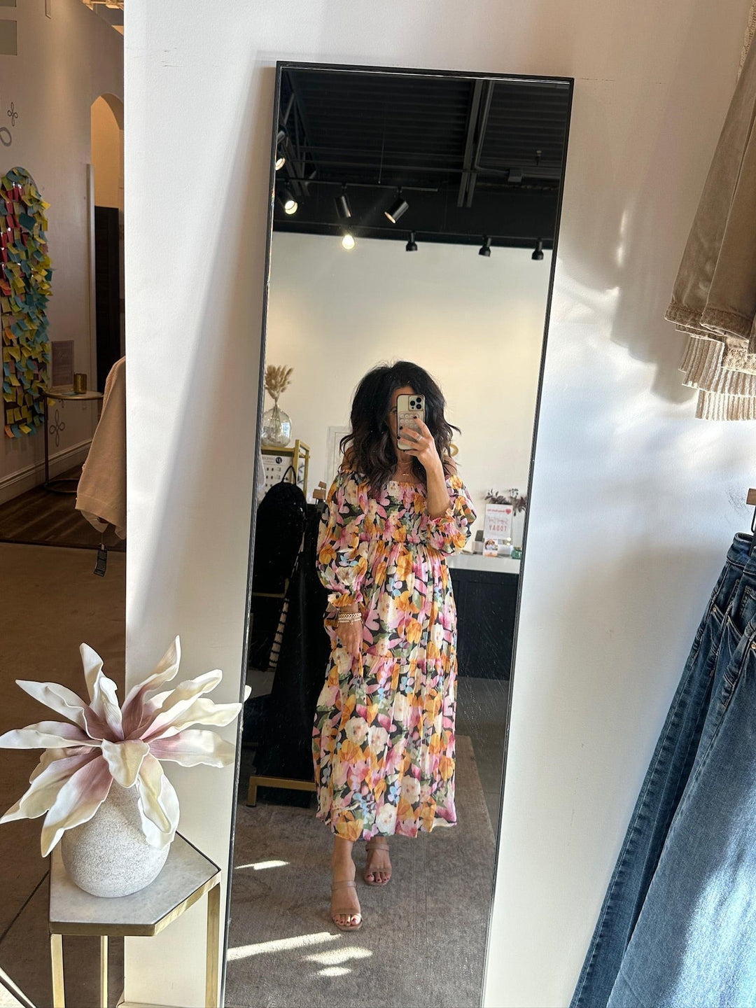 Person wearing a floral dress in a room with a mirror and clothing items.