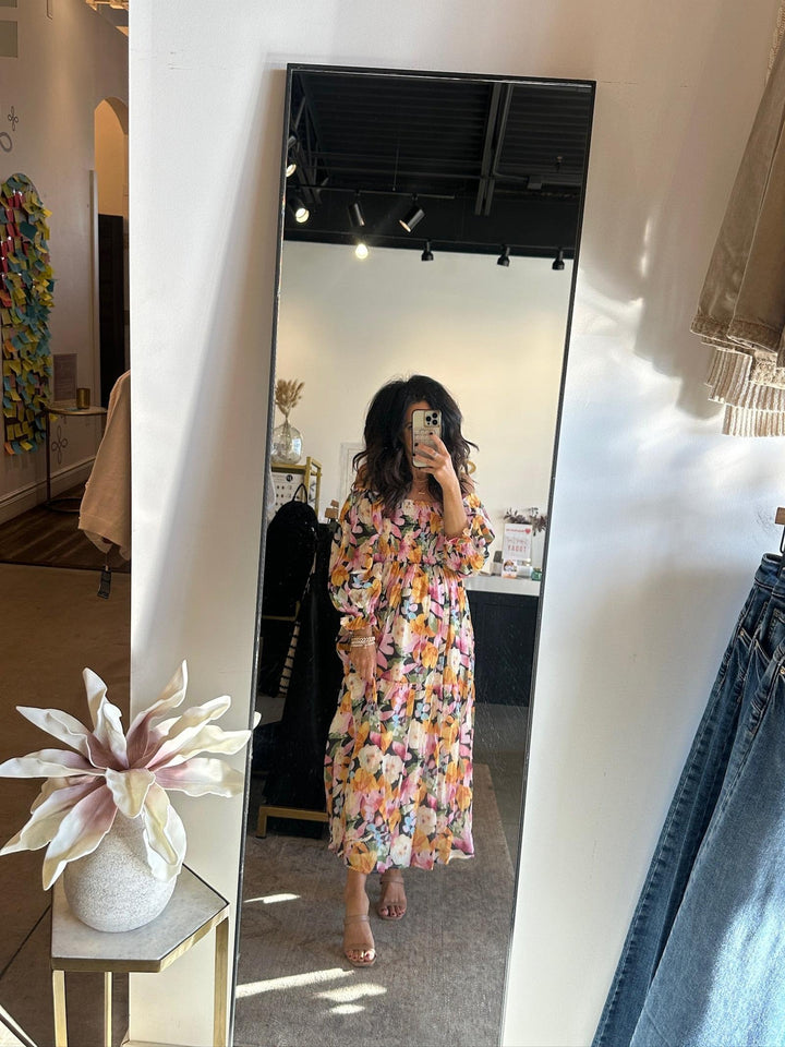 Person wearing a floral dress in a room with a mirror and clothing items.