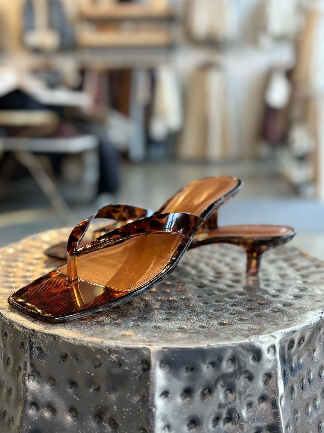 Pair of tortoiseshell sandals on a textured metal surface with a blurred indoor background.