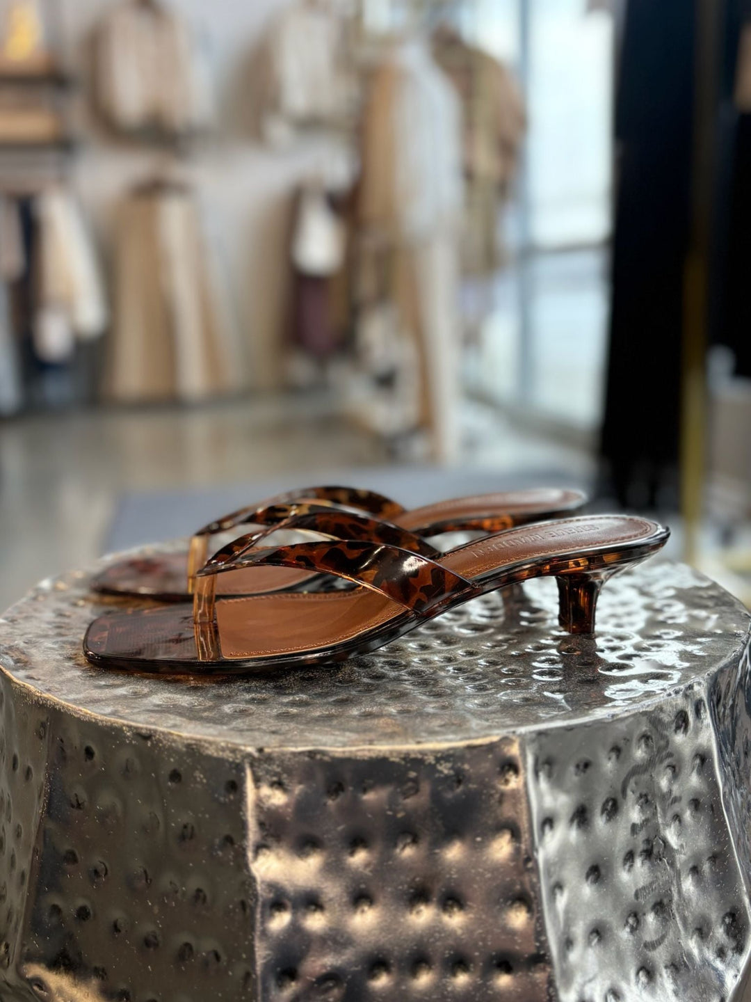 Pair of tortoiseshell sandals on a textured metal surface with a blurred indoor background.