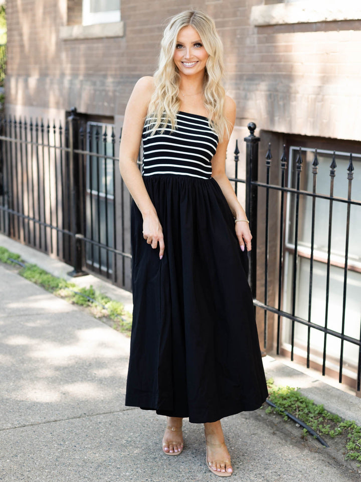 Woman wearing a black and white striped dress standing on a sidewalk.