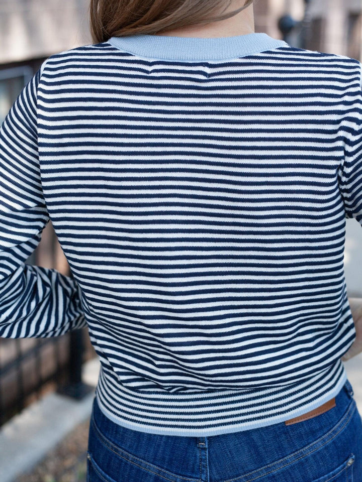 A person viewed from the back wearing a navy and white horizontally striped long-sleeve top with a light blue ribbed collar and hem, paired with blue jeans.