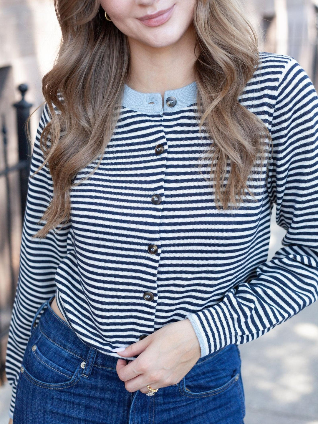 A woman wearing a navy and white horizontally striped long-sleeve button-up top with a light blue collar, paired with blue jeans.