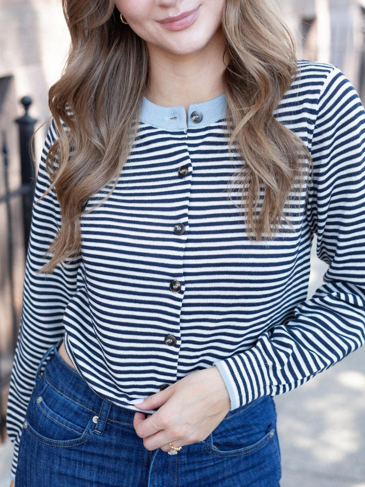 A woman wearing a navy and white horizontally striped long-sleeve button-up top with a light blue collar, paired with blue jeans.