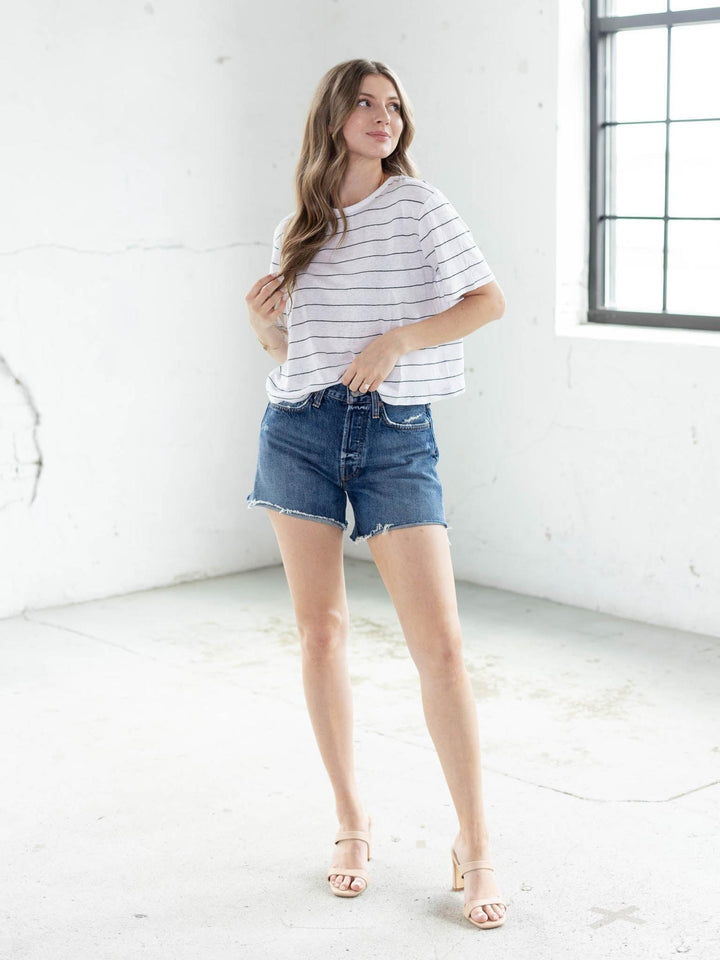 Woman wearing a white cotton-linen blend top with thin navy stripes, blue denim shorts, and nude heels.