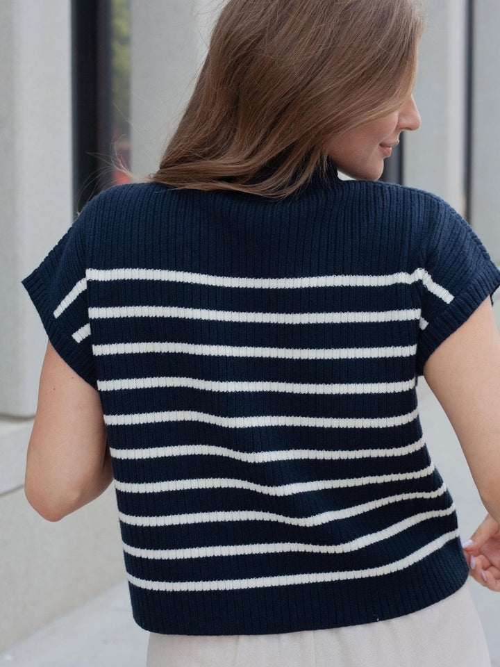 A woman shown from the back wearing a navy blue ribbed knit sweater with horizontal white stripes and short sleeves.