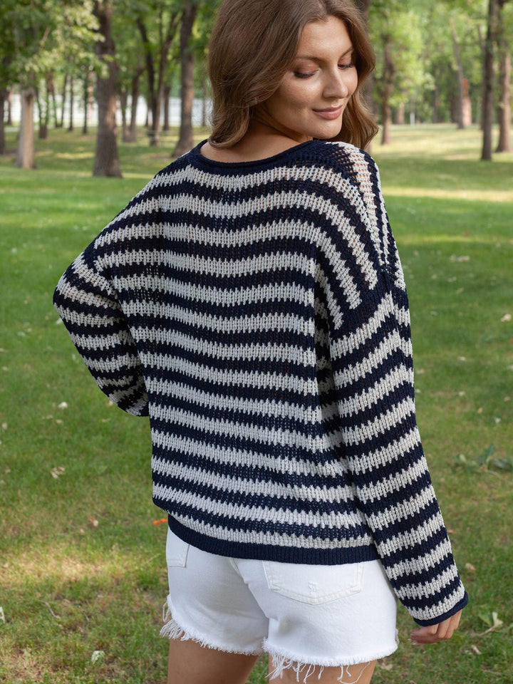 A woman wearing a navy blue and off-white horizontally striped knit sweater, shown from the back in an outdoor park setting with green grass and trees.