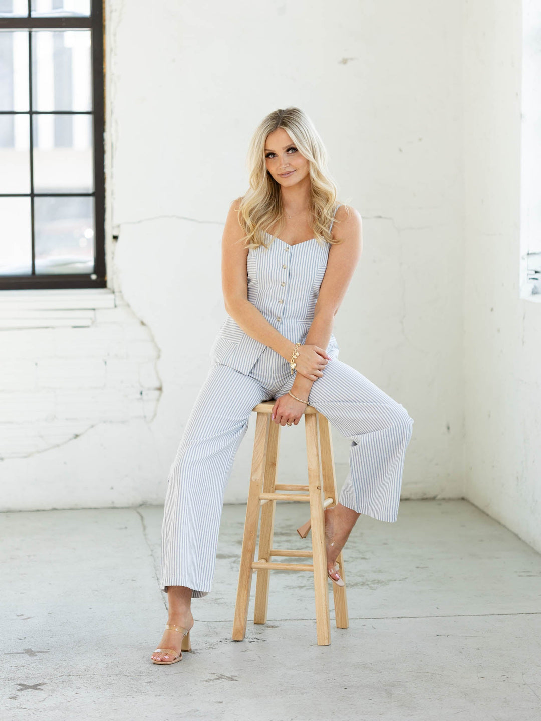Woman sitting on a wooden stool wearing a checkered outfit in a bright room.