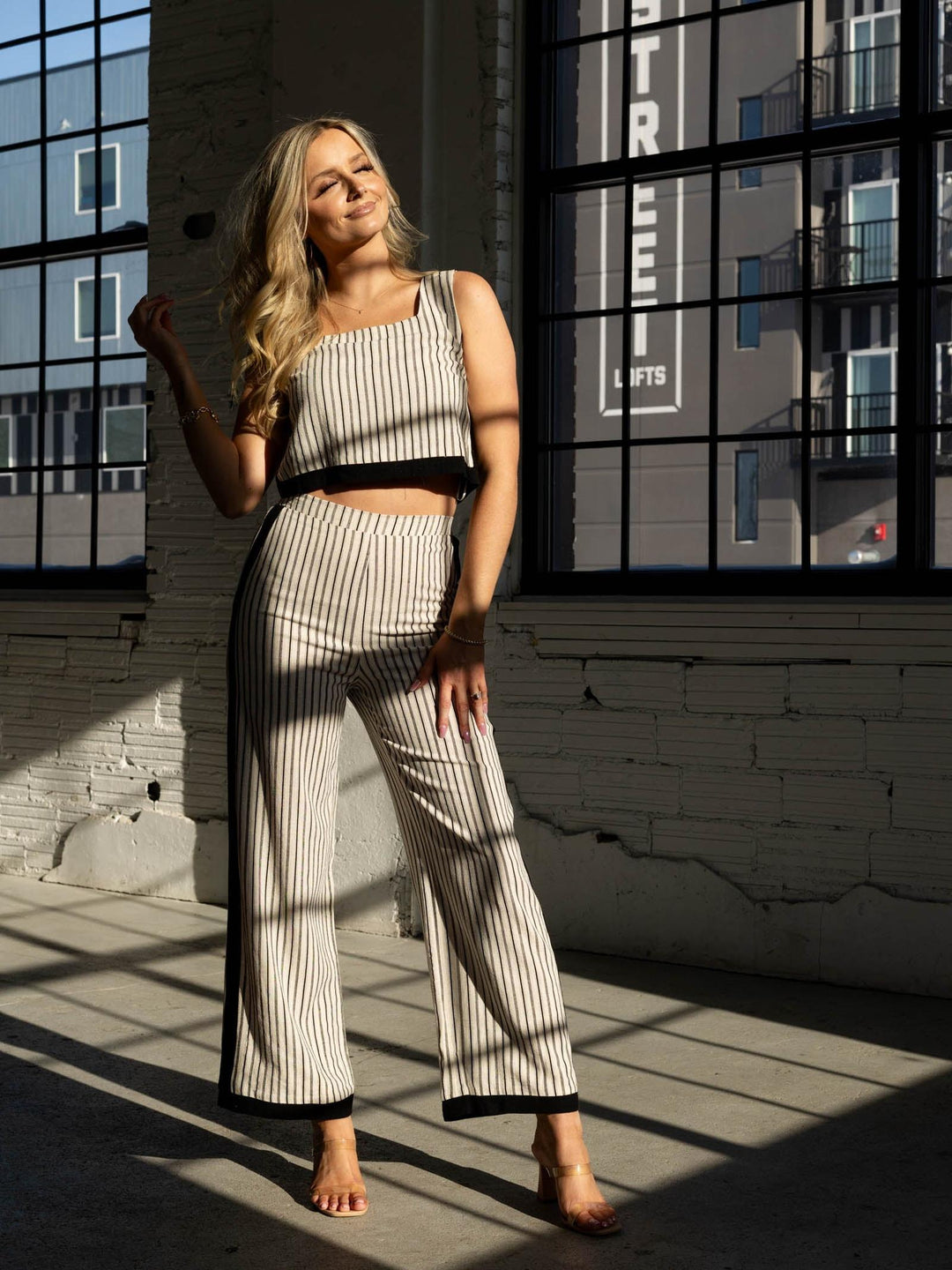 Woman in a striped outfit standing in front of large windows with a cityscape reflection.