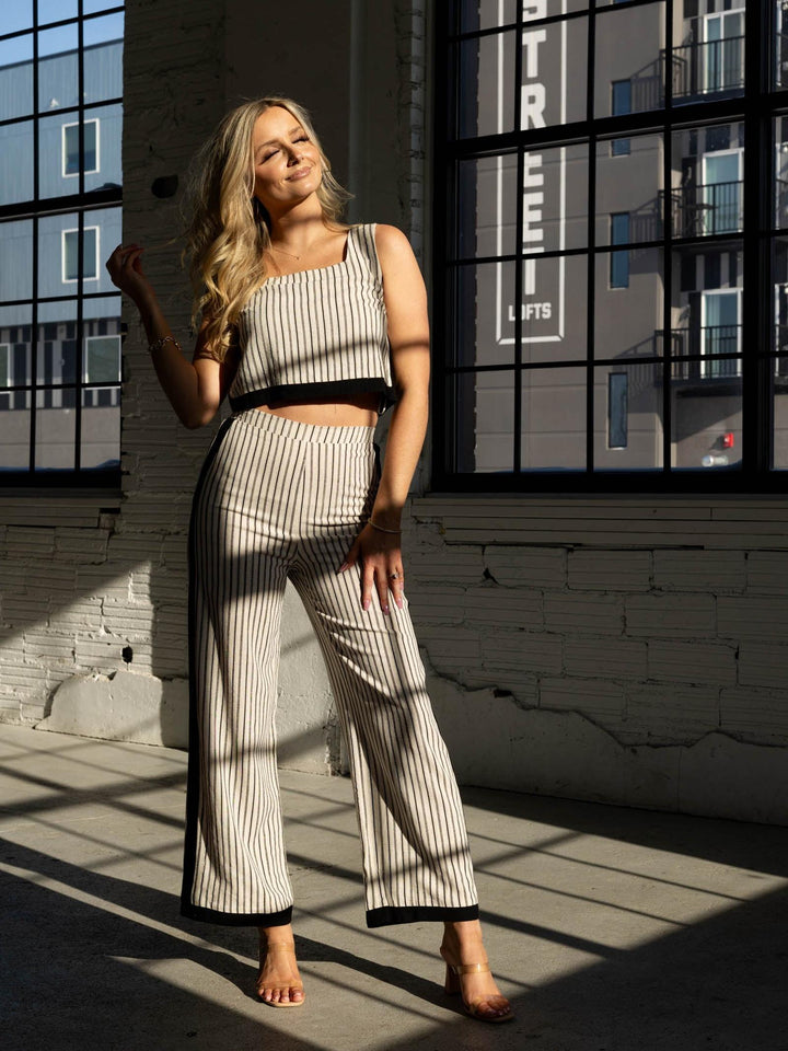 Woman in a striped outfit standing in front of large windows with a cityscape reflection.